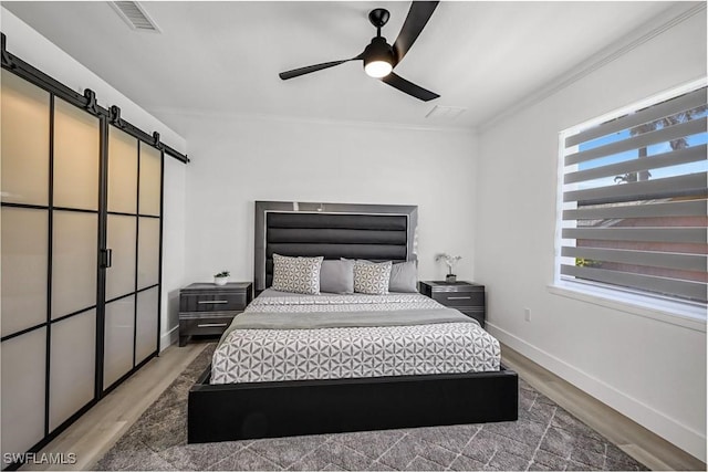 bedroom featuring a barn door, wood finished floors, crown molding, baseboards, and ceiling fan