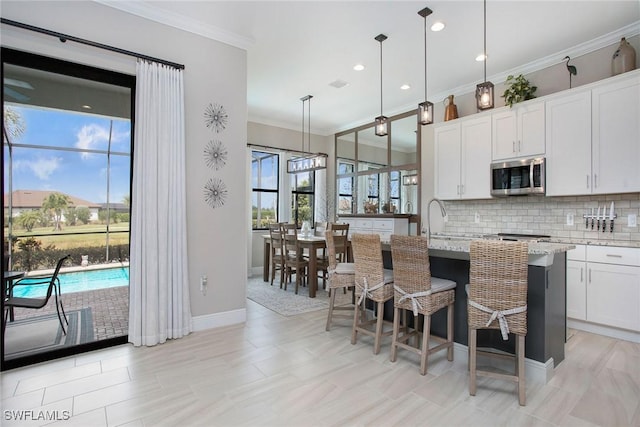 1421 Lucena Ln S, Naples, FL 34113 - kitchen with stainless steel microwave, crown molding, decorative backsplash, an island with sink, and light stone countertops