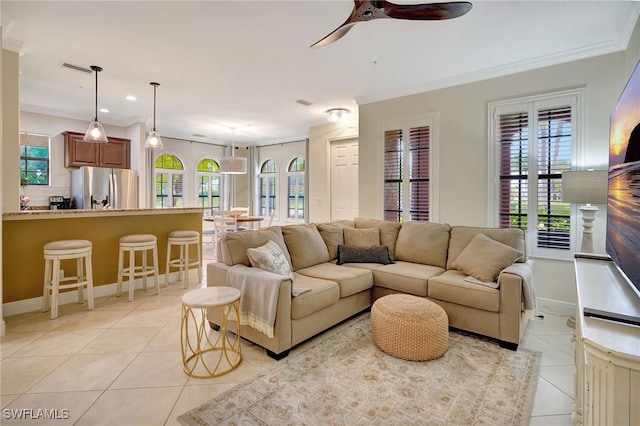 living area featuring light tile patterned flooring, ceiling fan, healthy amount of natural light, crown molding, and baseboards