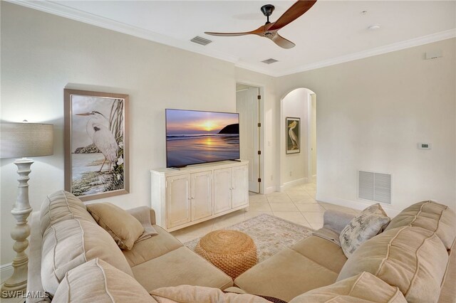 living area featuring a ceiling fan, arched walkways, light tile patterned floors, crown molding, and baseboards