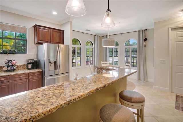 kitchen featuring stainless steel refrigerator with ice dispenser, ornamental molding, light stone counters, light tile patterned flooring, and decorative light fixtures