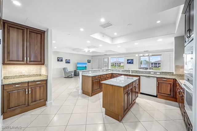 kitchen with white appliances, decorative backsplash, a kitchen island, light stone countertops, and light tile patterned floors