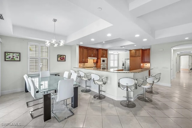 dining space with a tray ceiling, recessed lighting, light tile patterned floors, arched walkways, and baseboards