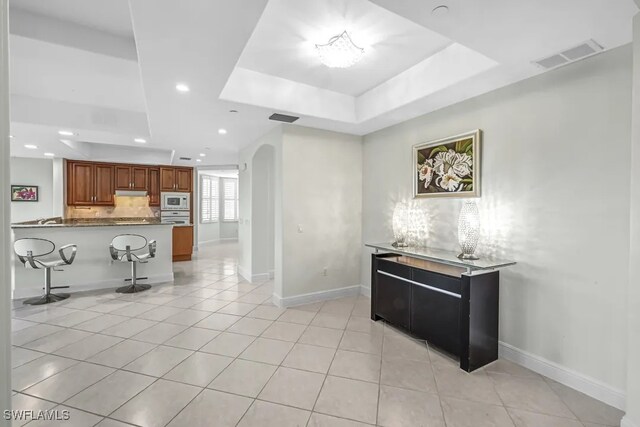 kitchen with white microwave, a tray ceiling, a breakfast bar, a peninsula, and under cabinet range hood