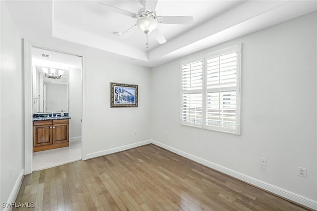 unfurnished bedroom featuring light wood-style floors, a tray ceiling, baseboards, and ensuite bathroom