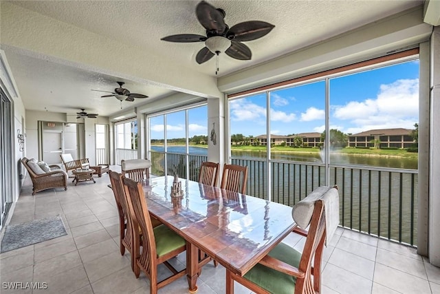 sunroom with ceiling fan, outdoor dining area, and a water view