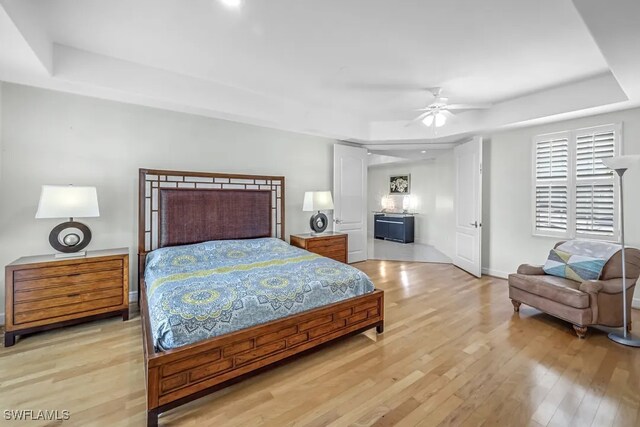 bedroom with a raised ceiling, light wood-style floors, baseboards, and ceiling fan