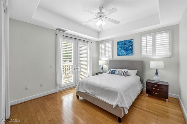 bedroom featuring a tray ceiling, access to outside, light wood-type flooring, and baseboards