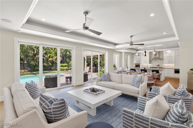 living area with a raised ceiling, ceiling fan, recessed lighting, baseboards, and light wood-style floors