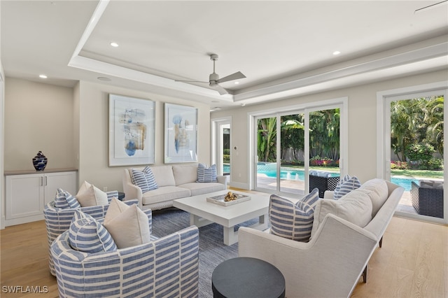 living area with a tray ceiling, recessed lighting, light wood-type flooring, and ceiling fan