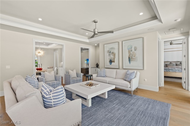 living room featuring a tray ceiling, light wood-style flooring, ceiling fan, recessed lighting, and baseboards