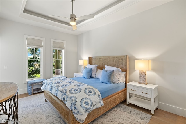 bedroom with light wood finished floors, a raised ceiling, baseboards, and ceiling fan