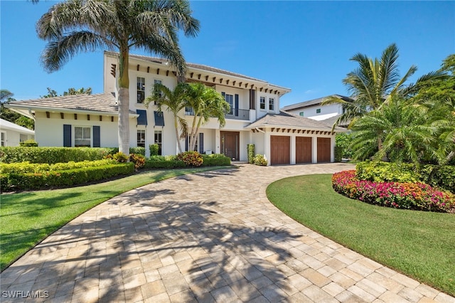 mediterranean / spanish-style house featuring decorative driveway, stucco siding, an attached garage, a front yard, and a balcony