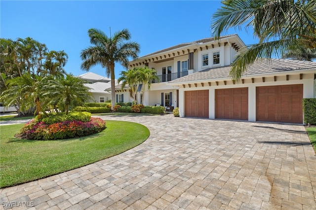 view of front of house featuring curved driveway, a balcony, stucco siding, and a front yard