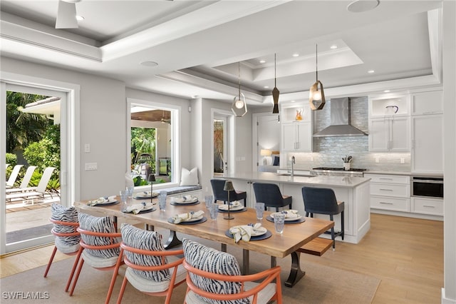 dining room with a tray ceiling, light wood-style floors, recessed lighting, and ornamental molding