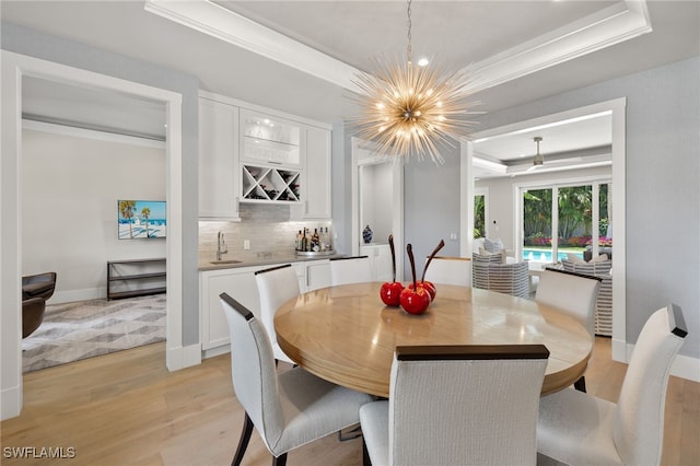 dining area featuring a raised ceiling, light wood-type flooring, ornamental molding, bar with sink, and a chandelier