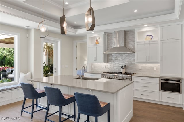 kitchen featuring wall chimney exhaust hood, a sink, a tray ceiling, backsplash, and recessed lighting