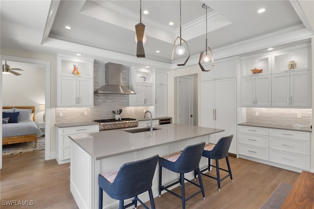 kitchen with wall chimney exhaust hood, a sink, a raised ceiling, backsplash, and recessed lighting