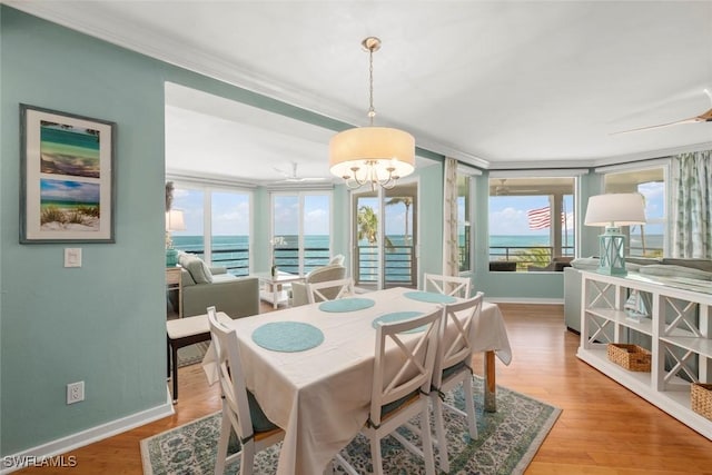 dining area featuring baseboards, a chandelier, wood finished floors, a water view, and crown molding