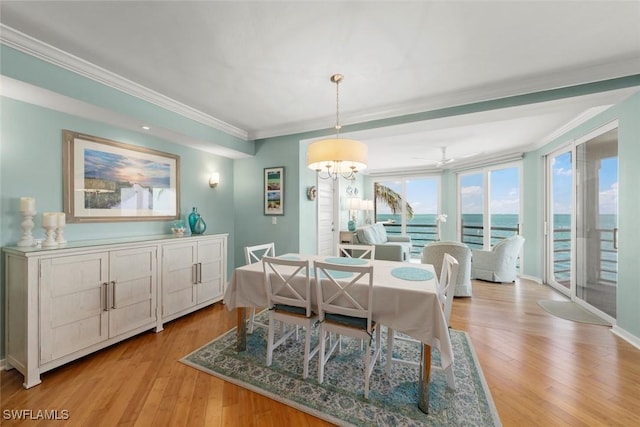 dining space featuring light wood-type flooring, ornamental molding, and a water view