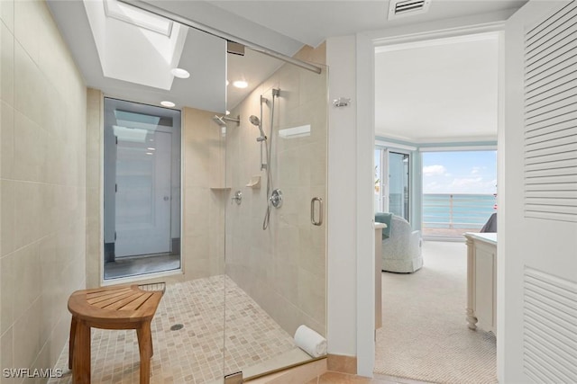 bathroom featuring a stall shower, a water view, a skylight, and recessed lighting