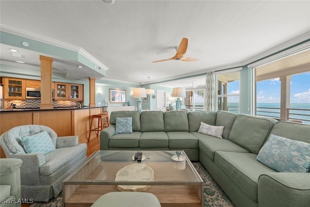 living room with a water view, crown molding, decorative columns, ceiling fan, and wood finished floors