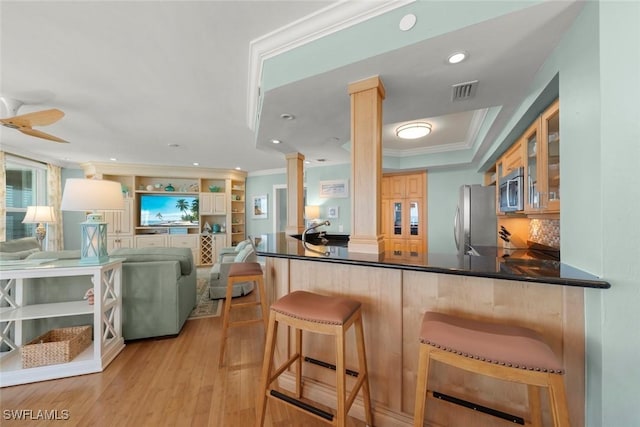 kitchen with decorative columns, stainless steel appliances, ornamental molding, glass insert cabinets, and light wood-style floors