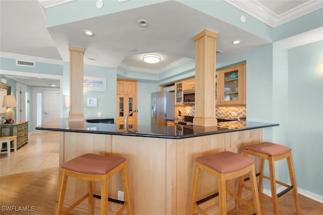 kitchen featuring appliances with stainless steel finishes, ornate columns, tasteful backsplash, crown molding, and glass insert cabinets