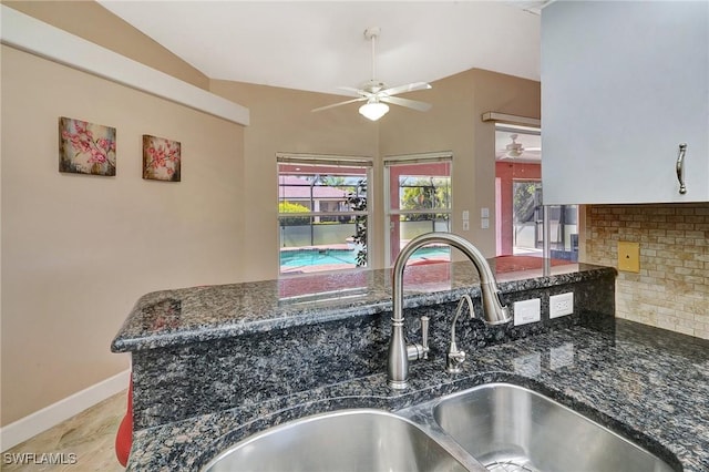kitchen view of ceiling fan, a sink, tasteful backsplash, baseboards, and dark stone countertops