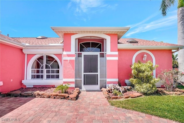 doorway to property with stucco siding and roof with shingles