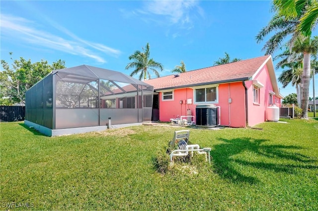 back of property with central AC unit, a yard, and glass enclosure