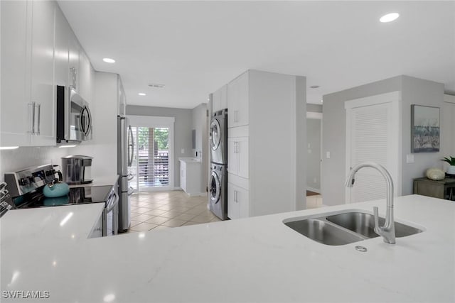 kitchen with appliances with stainless steel finishes, stacked washer / drying machine, a sink, recessed lighting, and light tile patterned flooring