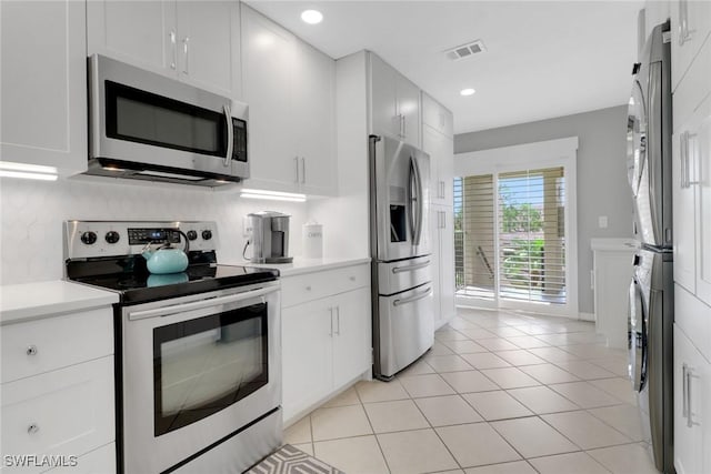 kitchen with appliances with stainless steel finishes, estacked washer and dryer, light countertops, white cabinets, and recessed lighting