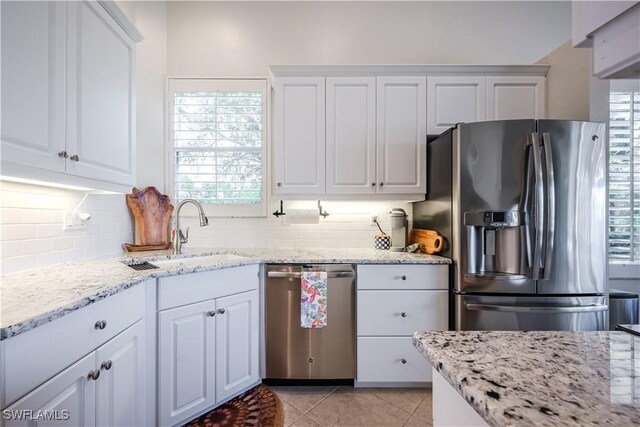 kitchen with stainless steel appliances, a sink, tasteful backsplash, white cabinetry, and light tile patterned floors