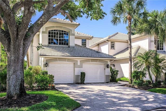 mediterranean / spanish home featuring stucco siding, a tile roof, and driveway