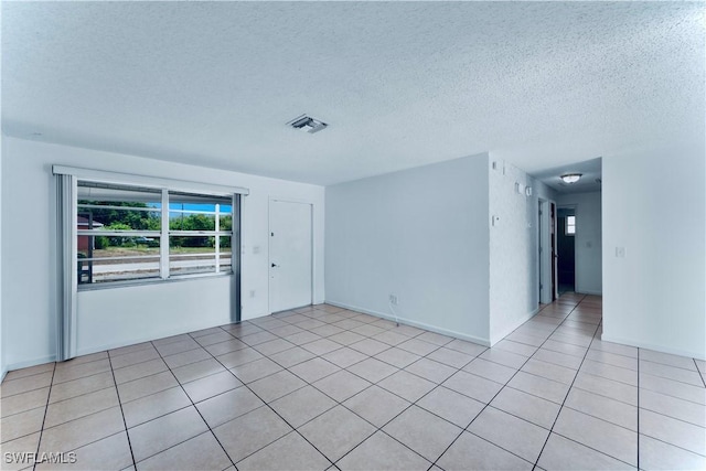 empty room with a textured ceiling and light tile patterned floors