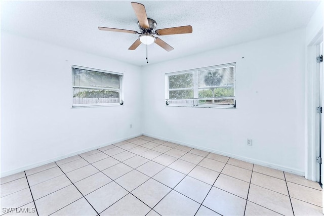 empty room featuring ceiling fan, light tile patterned flooring, baseboards, and a textured ceiling