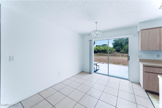 unfurnished dining area featuring a textured ceiling, a chandelier, baseboards, and light tile patterned floors