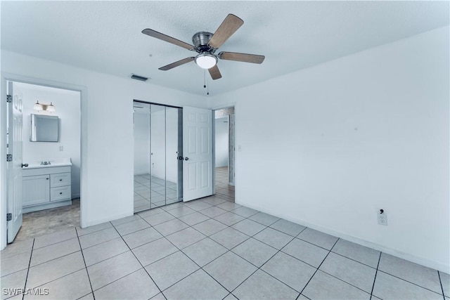 unfurnished bedroom with a closet, baseboards, ceiling fan, a sink, and light tile patterned floors