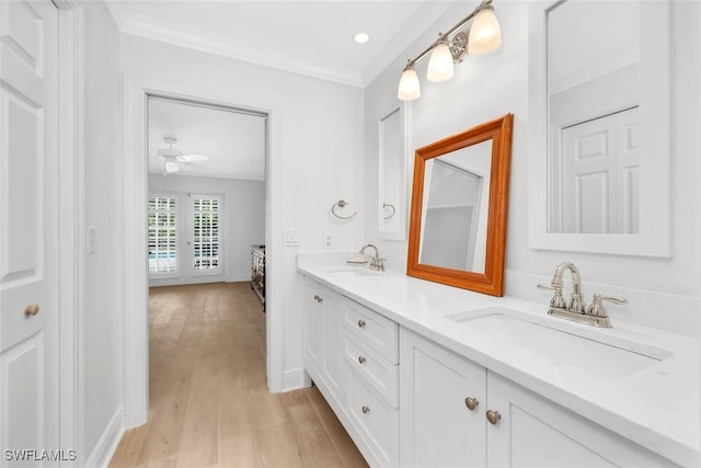bathroom with ornamental molding, wood finished floors, double vanity, ceiling fan, and baseboards