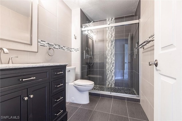 bathroom featuring tile walls, a textured ceiling, toilet, a shower stall, and vanity