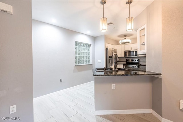 kitchen featuring a sink, dark stone counters, pendant lighting, white cabinets, and appliances with stainless steel finishes