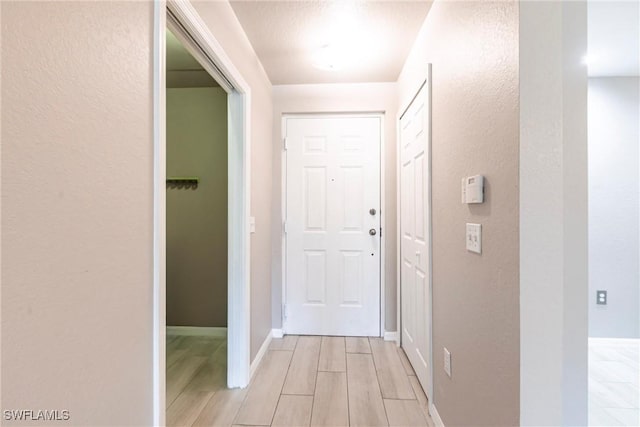 hallway with light wood finished floors, baseboards, and a textured wall