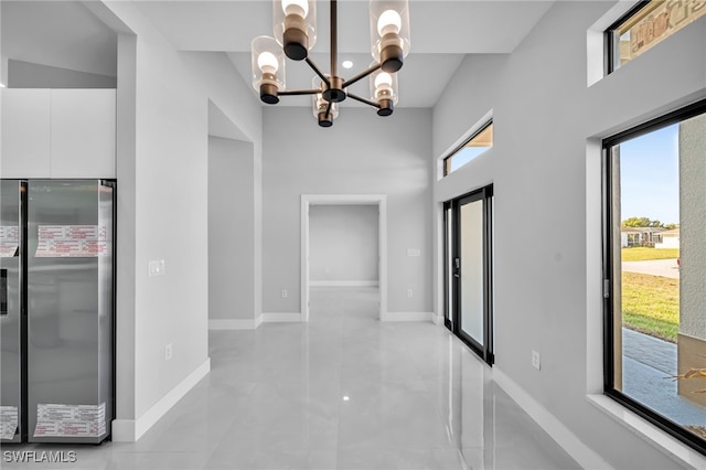 hallway featuring an inviting chandelier, elevator, baseboards, and a towering ceiling
