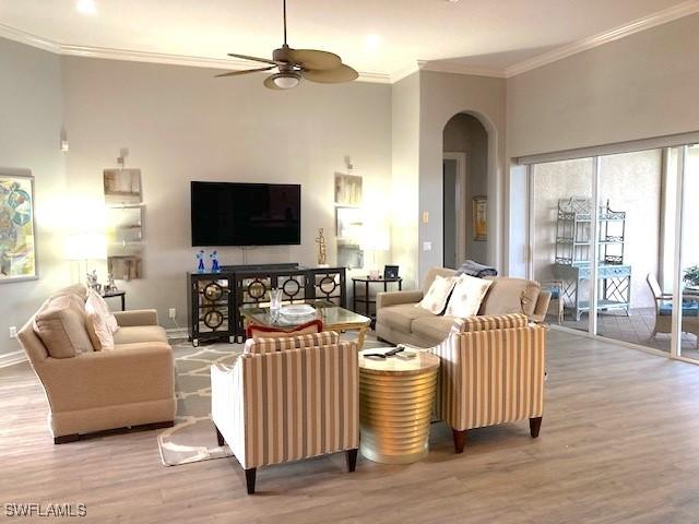 living room with crown molding, arched walkways, ceiling fan, wood finished floors, and baseboards