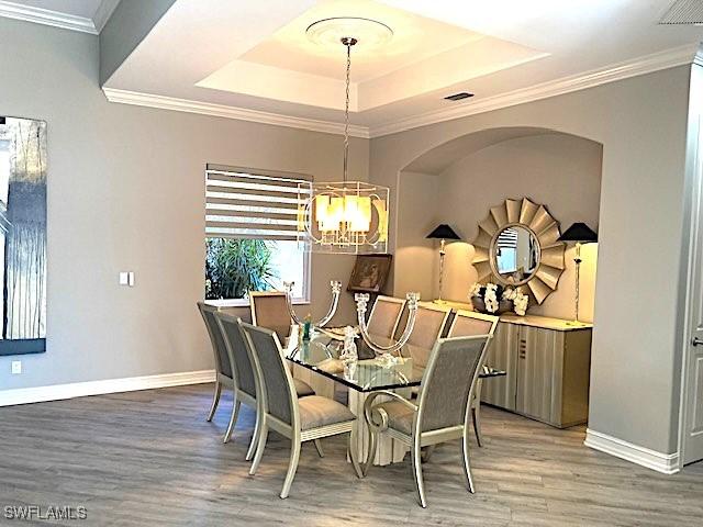 dining room featuring a chandelier, light wood-style floors, baseboards, crown molding, and a tray ceiling