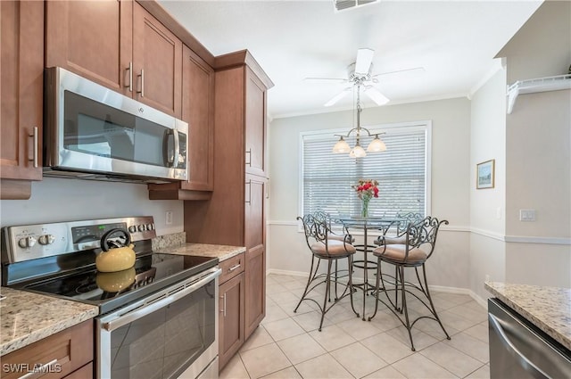 kitchen featuring stainless steel appliances, crown molding, brown cabinetry, a ceiling fan, and light stone counters