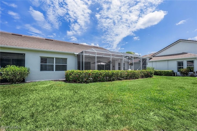 rear view of house featuring a lawn, stucco siding, and glass enclosure