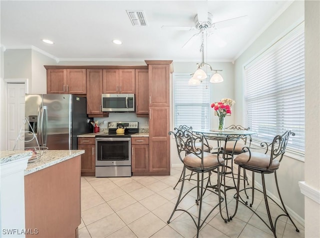 kitchen with appliances with stainless steel finishes, ornamental molding, a ceiling fan, brown cabinets, and light stone countertops