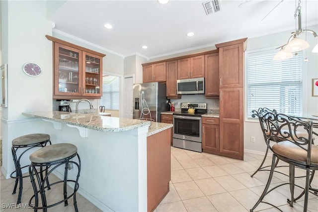 kitchen featuring appliances with stainless steel finishes, brown cabinets, a breakfast bar area, a peninsula, and light stone countertops